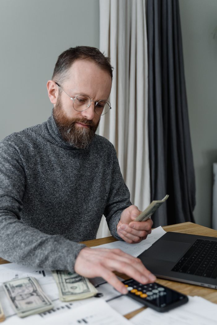 Businessman managing finances using calculator and cash indoors